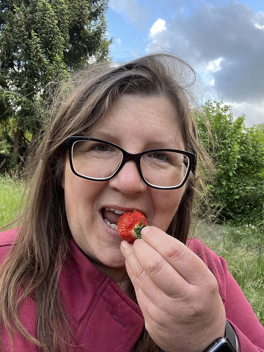 Eine Frau mit langen Haaren steckt sich eine Erdbeere in den Mund